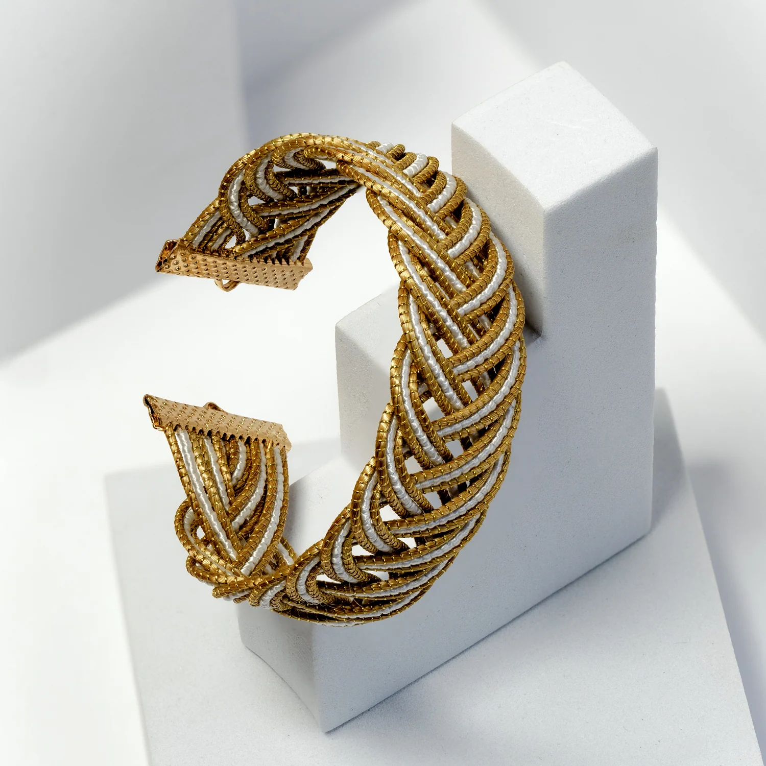 A woven cuff displayed on a pale jewellery stand.