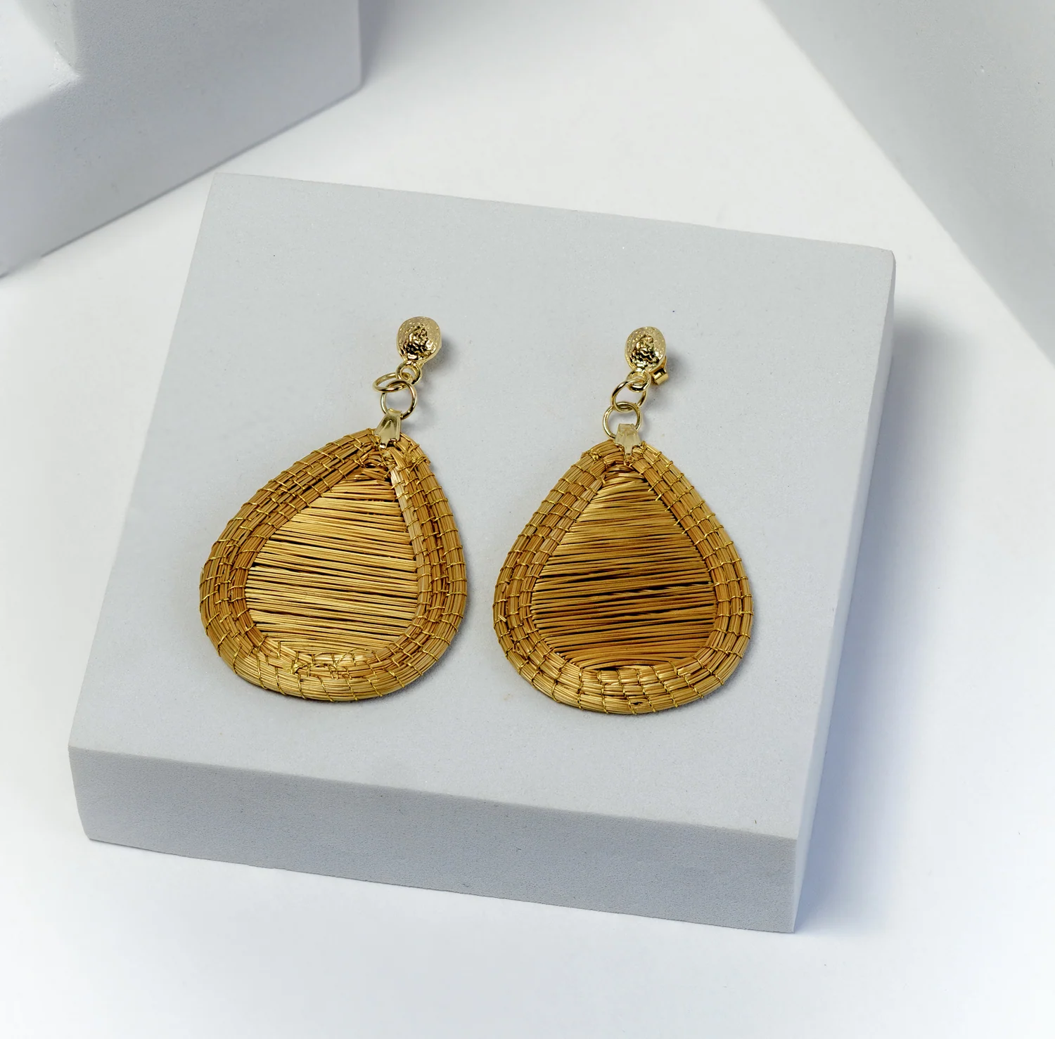 Teardrop-shaped woven earrings on a pale display block.